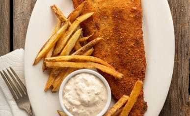 fried flounder with tartar sauce and homemade fries on the plate.