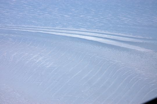 The white stripes are snow settled in the troughs of the ripples formed by the ice flowing around the nunatak. The fingerprint-like cracks in the foreground are crevasses bridged by snow lids. These crevasses are easily a few hundred feet across.