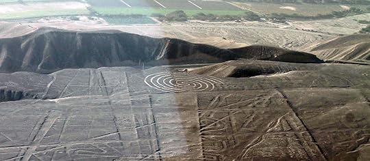 flat brown landscape with lines etched into it, before a ridge there is a distinct spiral visible that is etched into the ground, beyond the ridge are fields