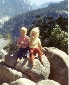 Two small children on a boulder in front of a valley view