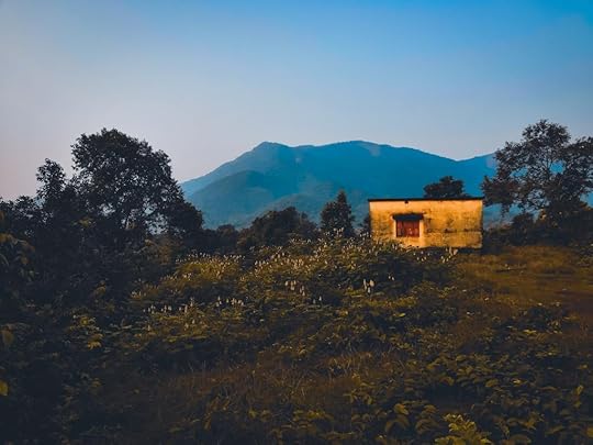 Photo of a small cabin in a grassy area with mountains in the background