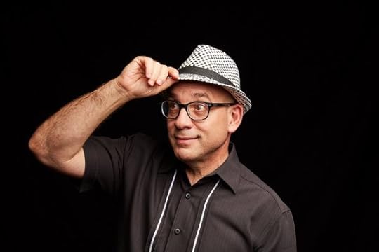Cal Fussman in a checkered trilby, standing in front of a black backdrop.