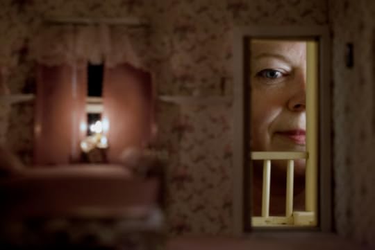 Image: inside of a dollhouse, with a woman looking in through the window