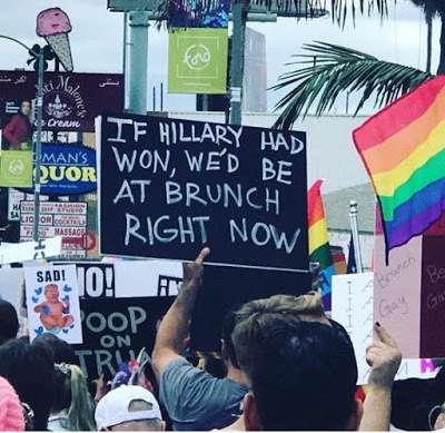 Photo of a protester holding a sign that says "IF HILLARY WON WE'D BE AT BRUNCH RIGHT NOW"