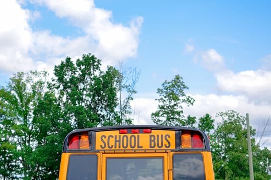 the back of a school bus against the backdrop of green leafy trees and a blue sky with wispy white clouds.