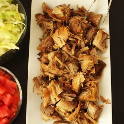 carnitas on platter next to bowls of tomatoes and lettuce