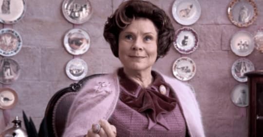 Umbridge in her office with her cat pictures & pink decorative wall.