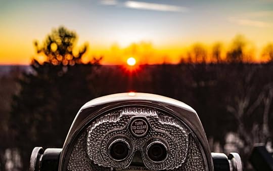 A tower viewer (binoculars on a stand) overlooks an out of focus horizon at sunset.
