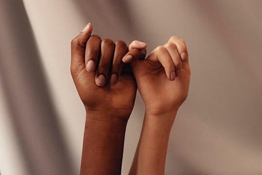An image of hands from two different women, one lighter-skinned, one darker-skinned, their pinkies are clasped.