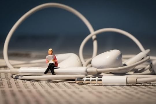 Image: miniature figure sitting atop a pair of wired earbuds, reading aloud