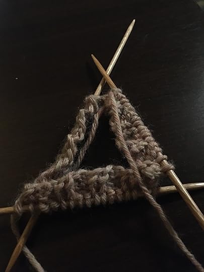 Three knitting needles with a few rows of stitches, laid in a triangular pattern.