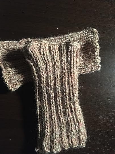 Completed wristers in khaki yarn, one laying on top of the other.