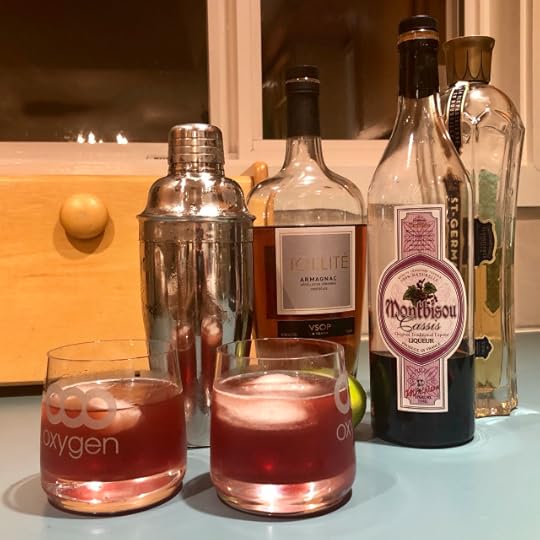 Photo of assorted bottles of spirits and liquers, cocktail shakers, lime, and two lowball glasses with ice and a dark red drink