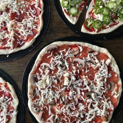 unbaked pizzas on screens on table