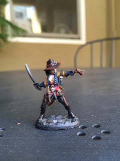 front view of a painted miniature woman figure pointing a crossbow and brandishing a sword