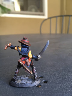back view of a painted miniature woman figure pointing a crossbow and brandishing a sword