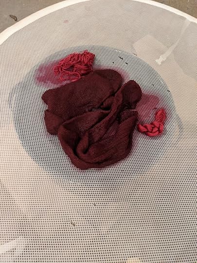 A photo of wet socks and thread draining on a mesh after being dyed red-purple.