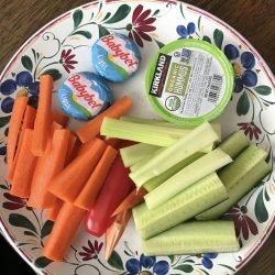 snacky lunch of veggies hummus and babybel cheese on flowered plate