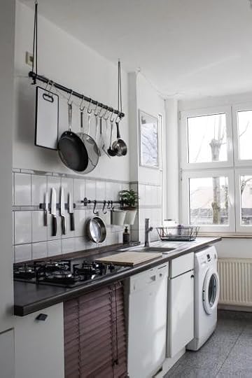 A small white kitchen with black countertops. There is a set of hooks with pans and other kitchen tools hung from them.