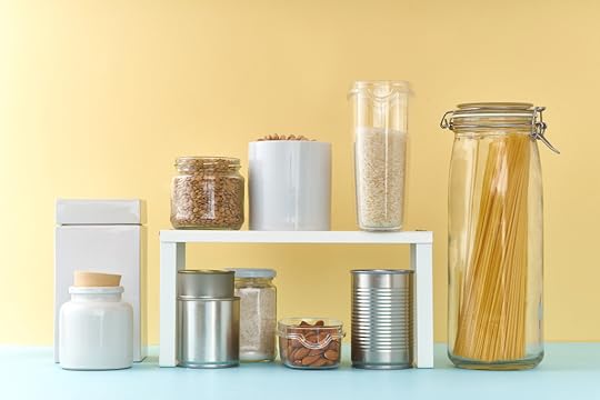 Pantry items on a light blue counter with a yellow wall behind. These items are demonstrating the use of a shelf organizer. 