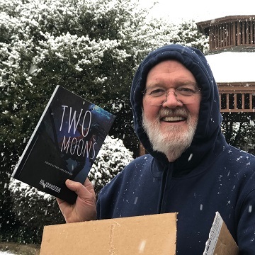 Hardcover of the novel Two Moons being opened by the author in snow.