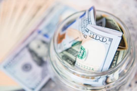 A glass jar filled with currency with a $100 bill prominently at the top.
