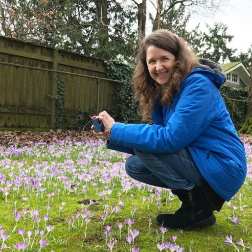 Me in my blue coat crouching in a field of crocuses, grinning at my husband who is taking a picture of me taking a picture