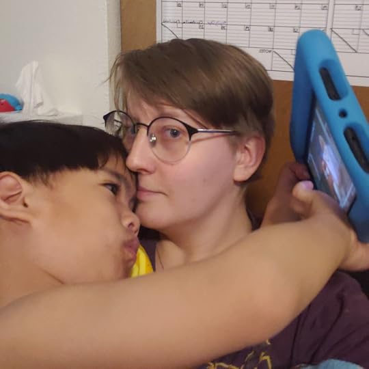 A child with black hair cuddles his mom while playing tablet.
