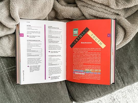 A photo of The Queens English, open to an inside page featuring a few entries from the letter H and an entry on LGBTQIA+ homelessness set on a bright red background.