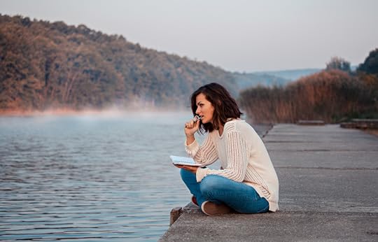 Writing worksheets can make pantsing a novel easier! A woman sits on the shore of a lake, writing a story.