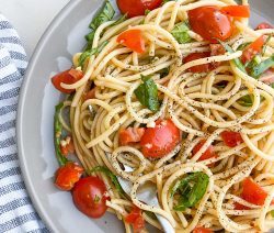 Close up of a plate of tomato basil pasta with a blue and white kitchen towel