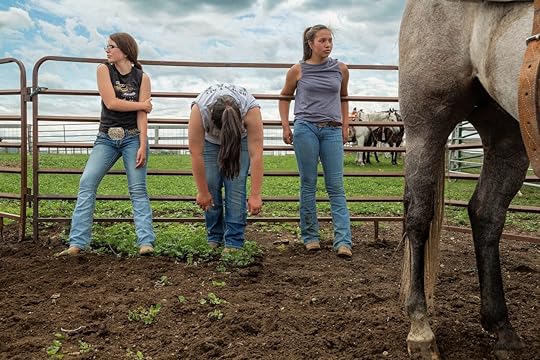 three girls in jeans standing along a horse enclosure railing