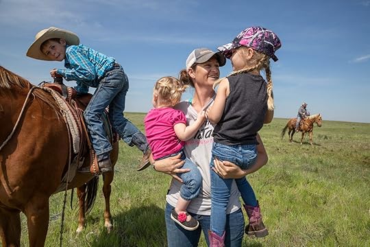 a woman holding two girls as a young boy gets off a horse