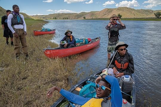 six young men along a riverside, sitting and standing in canoes