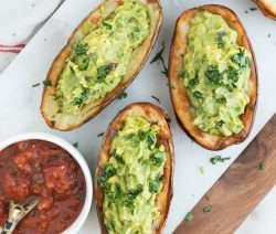 Three potato skins stuffed with guacamole with a small bowl on the side filled with salsa
