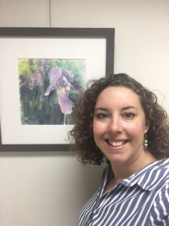 Watercolour artist Candice Leyland stands beside a watercolour painting of an iris (flower).