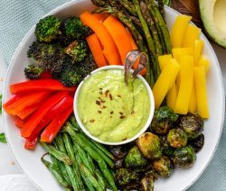 Bowl of colorful veggies with a small bowl of green avocado dressing