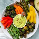 Bowl of colorful veggies with a small bowl of green avocado dressing