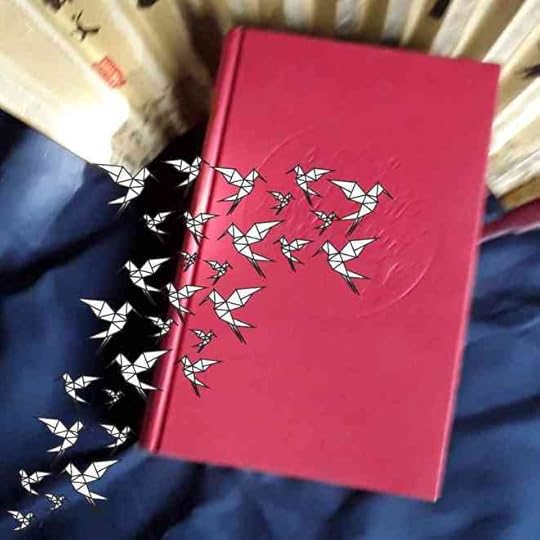 A red hardback copy of The Girl who Drank the Moon sits on the spine of a fan over a blue bakcground. White origami birds flock over it.