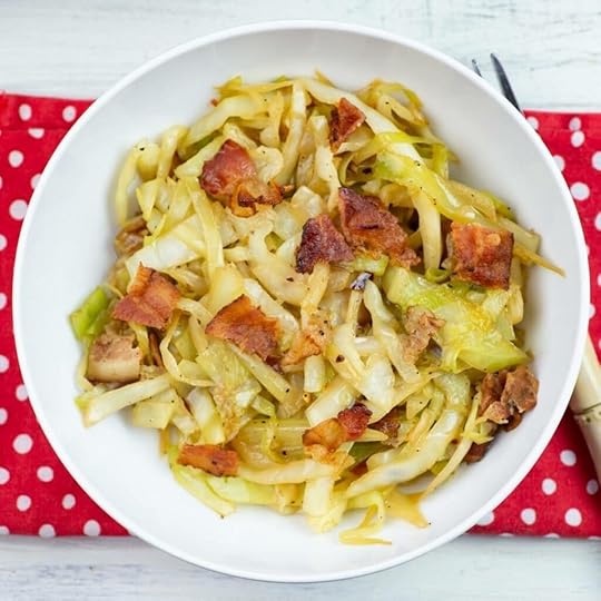 A white bowl filled with fried cabbage topped with crispy bacon pieces.