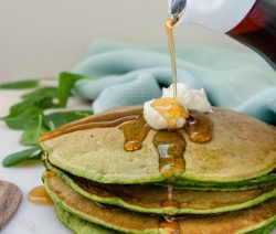 Stack of 4 green pancakes with a dollop of butter and maple syrup drizzling
