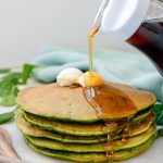 Stack of 4 green pancakes with a dollop of butter and maple syrup drizzling