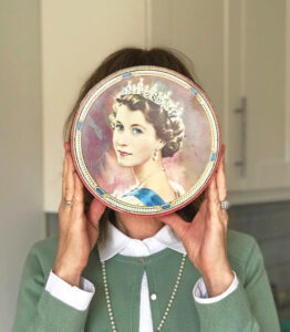 Woman holds vintage Queen Elizabeth cookie tin in front of face