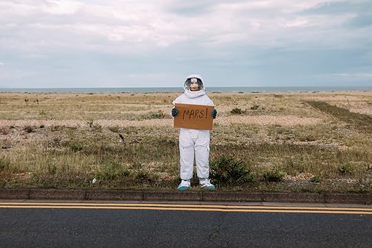 Astronaut hitchhiking at side of road with a sign saying