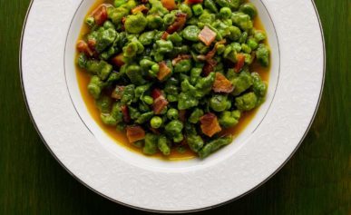 A bowl of spinach spaetzle with peas and bacon.