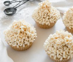 Four vegan vanilla cupcakes with vanilla frosting on a white surface