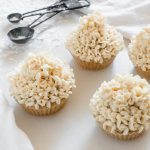 Four vegan vanilla cupcakes with vanilla frosting on a white surface