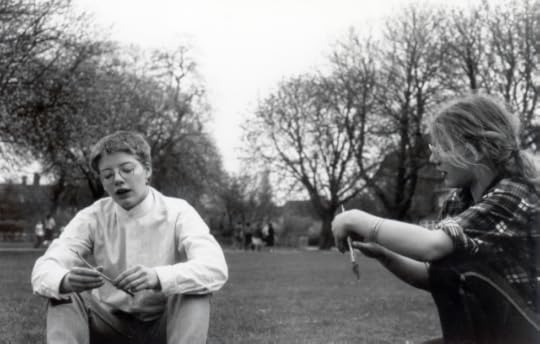 black and white photo of two sisters, one with short hair and one with long hair, in a park rolling cigarettes