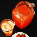 glass of pink lemonade with ice next to full pitcher