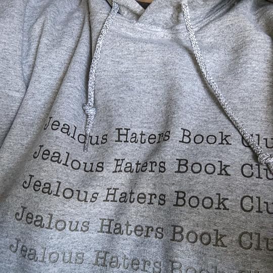 A close of a hoodie, with the collar and string things showing. Jealous Haters Book Club is printed multiple times in a column, again in varying shades of gray